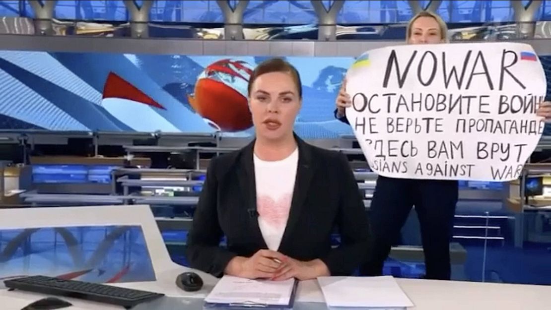 Eine Nachrichtensendung im russischen staatlichen Rundfunk. Im Hintergrund hält die Journalistin Maria Ovsyannikova ein Schild hoch mit der Aufschrift "NO WAR" und weiter in russischer Sprache "Stoppt den Krieg. Glauben Sie der Propaganda nicht. Hier belügen sie Sie."