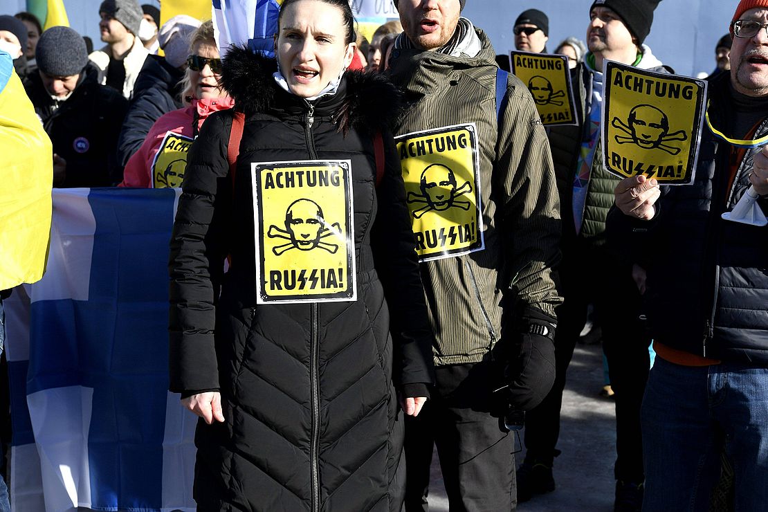 Demonstrierende mit Schildern mit der Aufschrift "Achtung RuSSia", wobei das Doppel-S als doppelte Sigrune geschrieben ist (in Anspielung auf die Waffen-SS der Nazis).