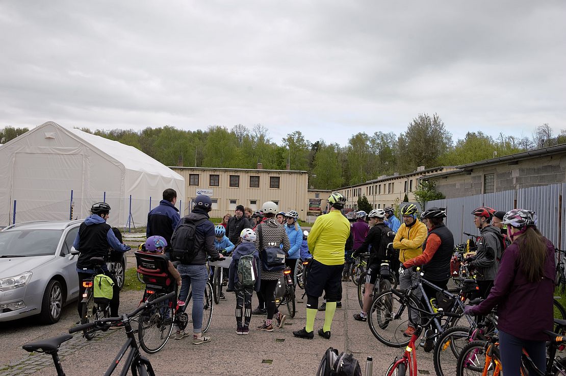 Die Gruppe bei einer Station der Radtour. Im Hintergrund sieht man die in der Bildbeschreibung erwähnten Baracken. 