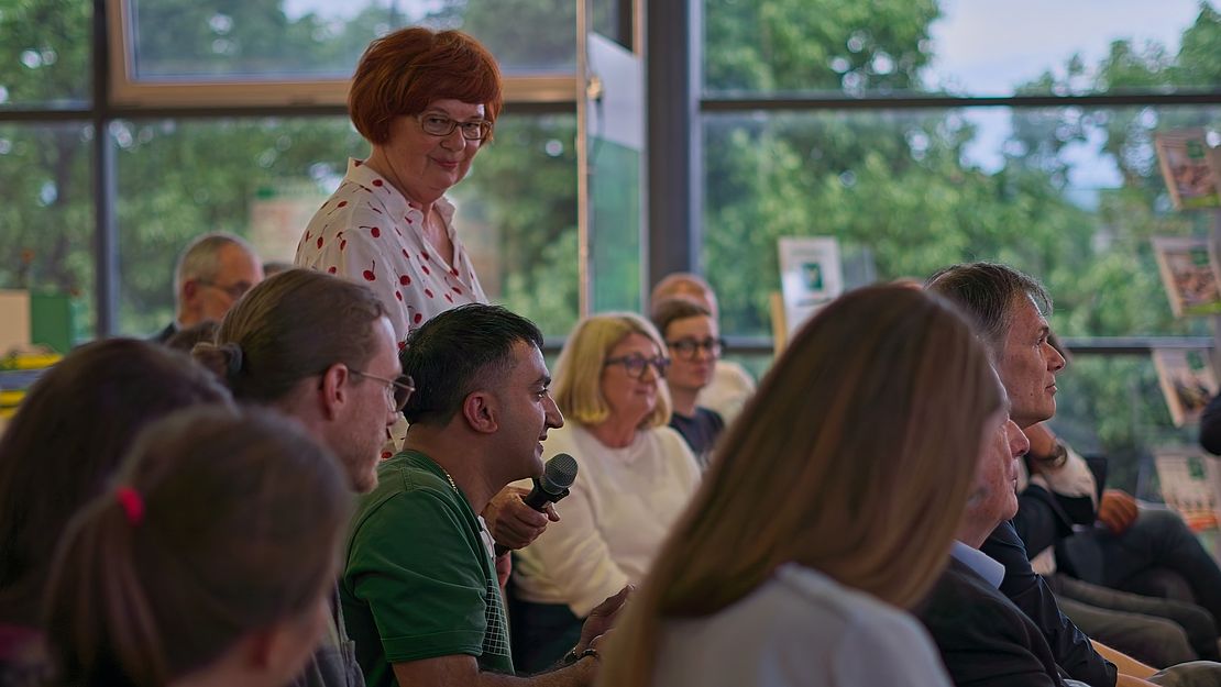 Person mit Mikrofon stellt Frage in einer offenen Fragerunde, Publikum hört aufmerksam zu, Diskussion über Zukunftsfragen