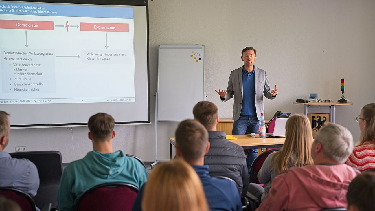 Prof. Dr. Tom Thieme erläutert während eines Vortrags Inhalte zum Thema Demokratie und Extremismus. Die Teilnehmenden verfolgen den Vortrag im Seminarraum.