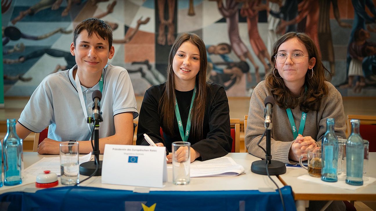 Drei Personen sitzen nebeneinander an einem Tisch. Vor ihnen Mikrofone und ein Schild mit der Aufschrift "Präsidium des Europäischen Rates".