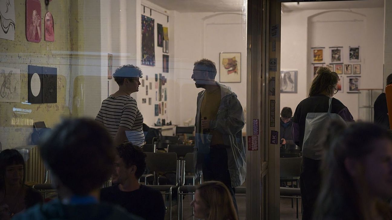 menschen sitzen vor dem schaufenster des hole of fame. eine person steht in der tür, zwei andere sprechen auf der anderen seite des fensters im raum miteinander.