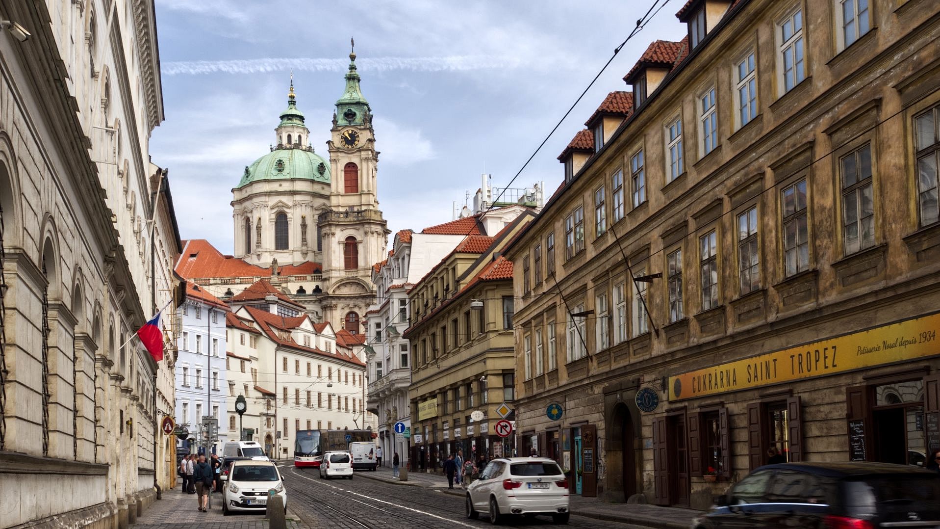 Bild einer prager Staße mit Geschäften. Im Hintergrund steht die Kuppel einer Kirche.