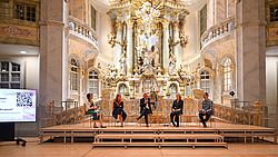 11.09.26_slpb_USA_Frauenkirche_Foto_AnjaSchneider Fünf Personen sitzen auf Stühlen vor einer barocken Altarwand in der Frauenkirche Dresden.