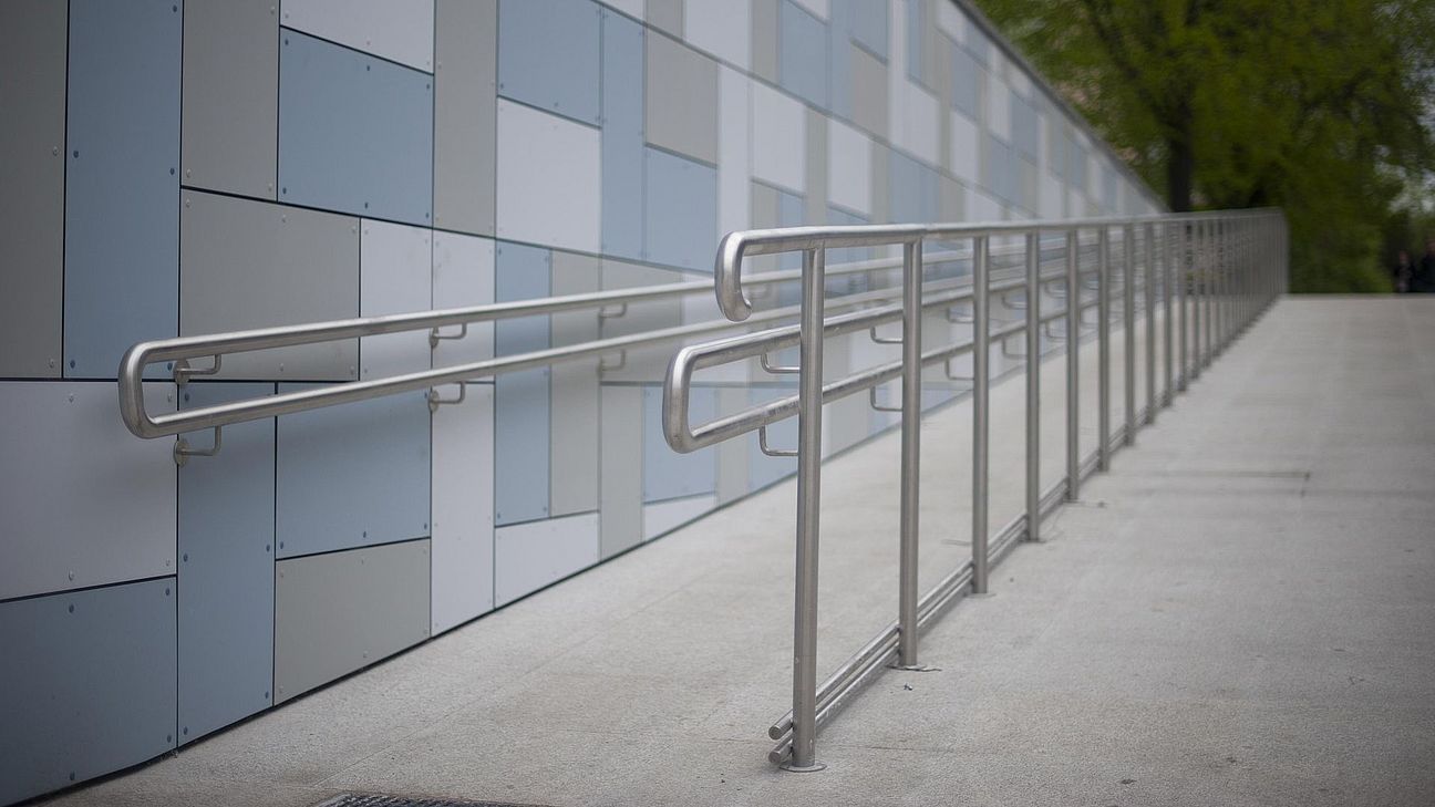 Im Vordergrund führt eine Rampe mit Haltegriffen in den Hintergrund. Dort stehen Bäume.