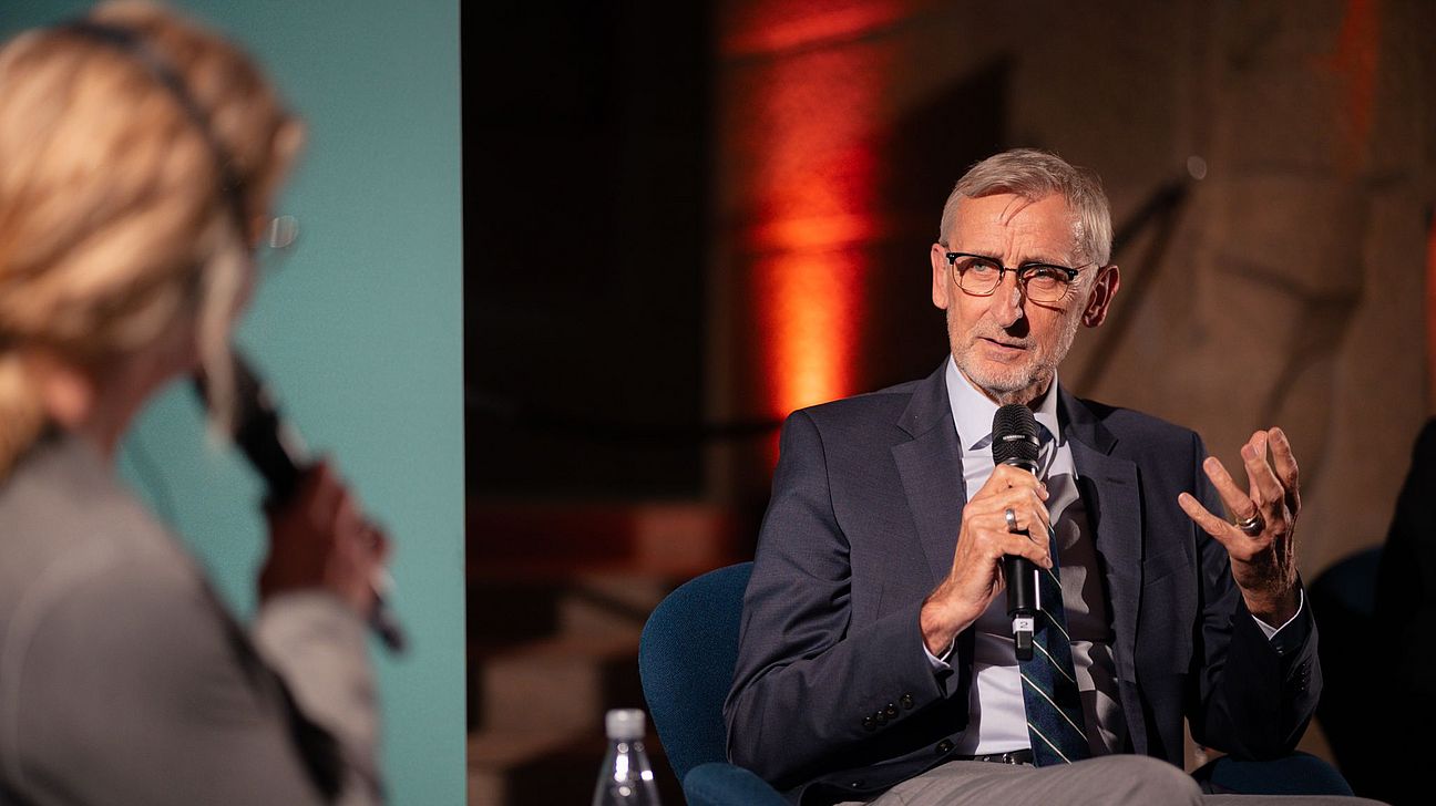 Sächsischer Innenminister Schuster in Anzug und Krawatte spricht mit Mikrofon, Moderatorin Dippmann mit Mikrofon im Vordergrund, Veranstaltung im Leipziger Völkerschlachtdenkmal.