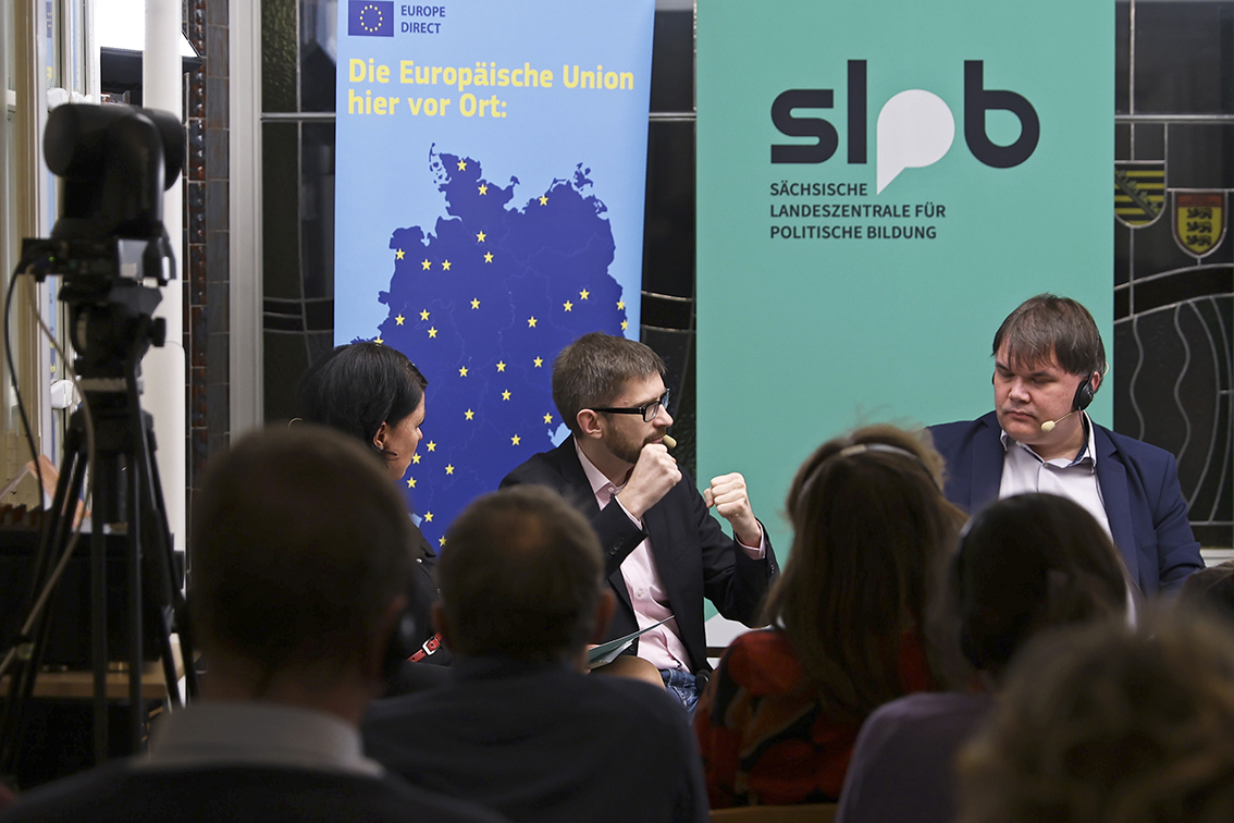 Podiumsdiskussion mit drei Personen vor Bannern der Europäischen Union und der Sächsischen Landeszentrale für politische Bildung, Publikum im Vordergrund.
