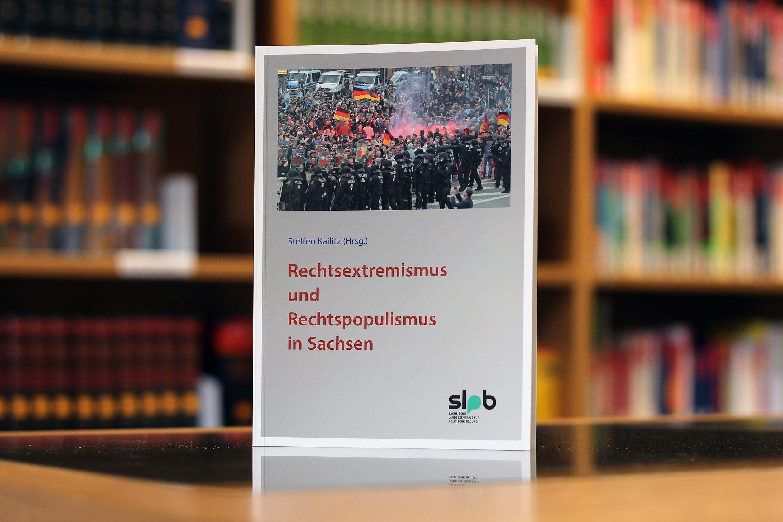 Zu sehen ist ein Buchcover mit dem Titel "Rechtsextremismus und Rechtspopulismus in Sachsen". Der Herausgeber des Buches ist Steffen Kailitz. Das Buch wird verlegt von der "Sächsische Landeszentrale für politische Bildung" und vom "Vandenhoeck & Ruprecht Verlag". Das Coverbild zeigt eine Menschenmenge bei einer Versammlung mit Polizeipräsenz im Hintergrund. Bei Klick vergrößert sich das Bild.